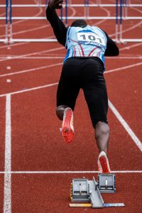 Atleta de atletismo posicionado na linha de partida, prestes a iniciar uma corrida. A imagem destaca a importância dos sapatos esportivos e forros específicos para melhorar o desempenho nas competições. Explore como os forros para calçados podem influenciar a performance dos atletas em corridas de alta intensidade.